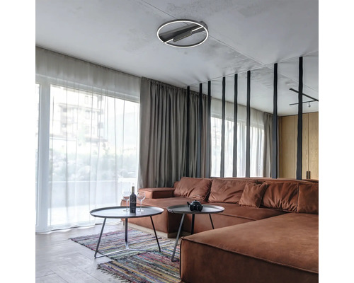 Sufragerie modernă cu plafonieră LED circulară, canapea mare maro și măsuțe de cafea rotunde în fața ferestrelor de la podea la tavan.