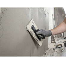 Artizan care nivelează un perete cu o gletieră și chit.