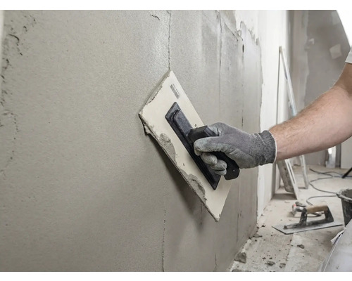 Artizan care nivelează un perete cu o gletieră și chit.