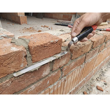 Artizan care lucrează la un zid de cărămidă cu mistrie de rosturi