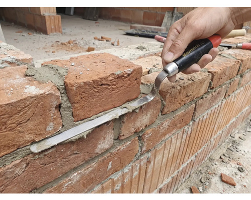 Artizan care lucrează la un zid de cărămidă cu mistrie de rosturi