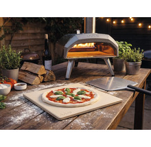 Imagine exterioară cu un cuptor de pizza Ooni cu pizza, paletă de pizza și ingrediente pe o masă de lemn.
