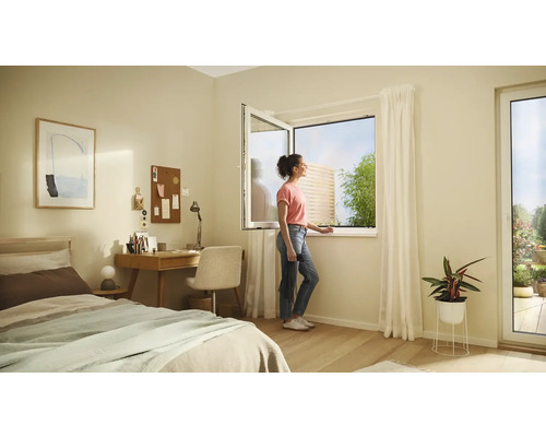 Dormitor luminos cu pat, birou și o femeie care deschide o fereastră cu vedere la grădină.