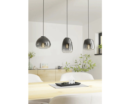 Trei lămpi suspendate din sticlă deasupra unei mese din lemn într-o cameră luminoasă