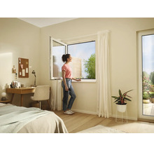 Cameră luminoasă cu fereastră deschisă, birou, pat și o femeie care se uită pe fereastră