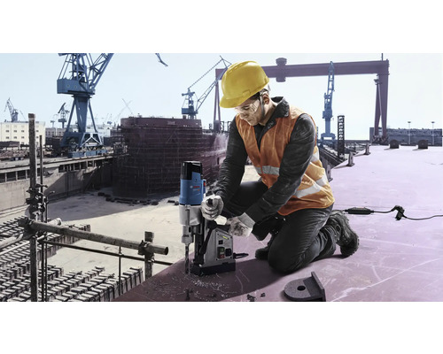 Un muncitor folosește o mașină de găurit cu carotă magnetică pe un șantier.