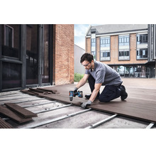 Un bărbat montează scânduri de terasă cu o șurubelniță cu acumulator în aer liber.