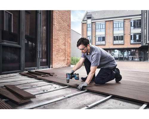 Un bărbat montează scânduri de terasă cu o șurubelniță cu acumulator în aer liber.