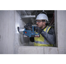 Un muncitor în construcții găurește un perete de beton cu un ciocan rotopercutor cu acumulator.