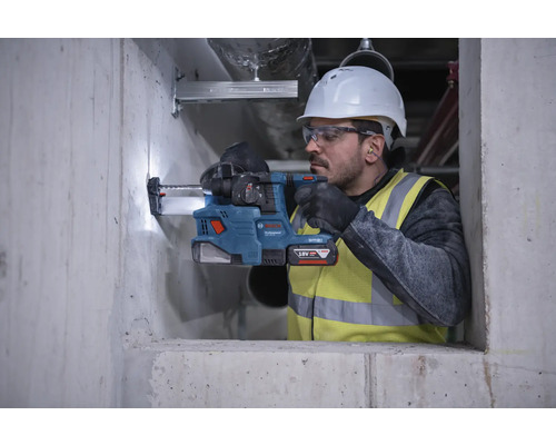 Un muncitor în construcții găurește un perete de beton cu un ciocan rotopercutor cu acumulator.