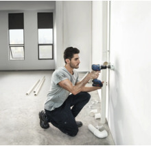 Un bărbat găurește un perete cu o mașină de găurit cu acumulator pentru o țeavă.