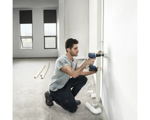 Un bărbat găurește un perete cu o mașină de găurit cu acumulator pentru o țeavă.
