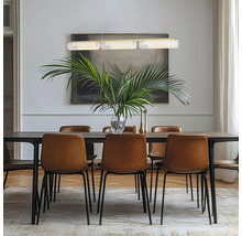 Sufragerie modernă cu masă din lemn închis, scaune din piele maro și pendulă cu trei abajururi din sticlă deasupra unei plante de palmier.