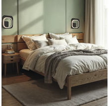 Dormitor modern cu pat din lemn, lenjerie albă, pătură gri, aplice de perete pătrate și noptieră din lemn pe un perete verde deschis.