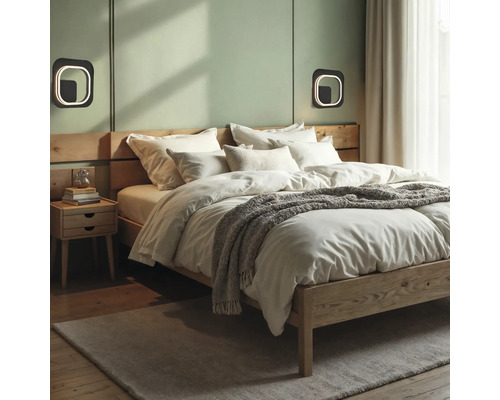 Dormitor modern cu pat din lemn, lenjerie albă, pătură gri, aplice de perete pătrate și noptieră din lemn pe un perete verde deschis.