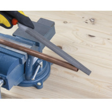 O țeavă de cupru este prelucrată cu o pilă fixată într-o menghină.