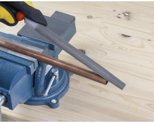 O țeavă de cupru este prelucrată cu o pilă fixată într-o menghină.