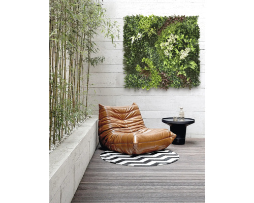 Scenă cu un fotoliu, o masă, un covor rotund și un panou de perete verde pe o terasă