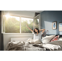 Dormitor luminos cu fereastră din plastic larg deschisă prin care intră lumina soarelui și o persoană care se întinde în pat la trezire.