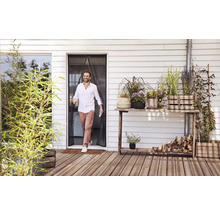 Un bărbat trece printr-o perdea magnetică împotriva insectelor la o ușă de terasă pe o terasă din lemn cu diverse plante la ghiveci.