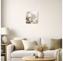 Oglindă de perete pătrată cu colțuri rotunjite într-o cameră de zi luminoasă, deasupra unei canapele cu perne decorative.