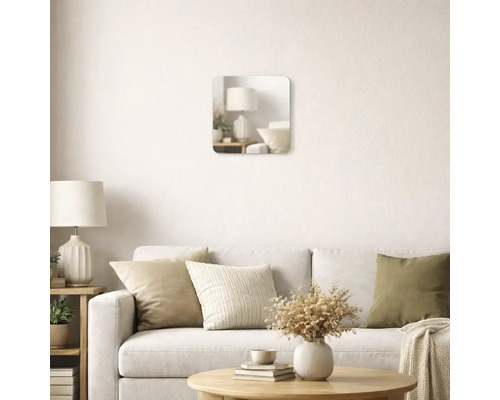 Oglindă de perete pătrată cu colțuri rotunjite într-o cameră de zi luminoasă, deasupra unei canapele cu perne decorative.