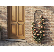 Spalier din metal cu motive de păsări și frunze, cu trandafiri cățărători pe un perete de cărămidă lângă o ușă din lemn.