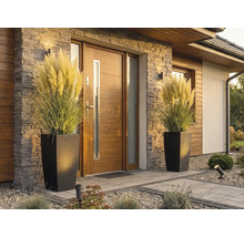 Intrare modernă în casă cu ușă din lemn, placare cu piatră și două ghivece înalte cu aspect de ratan și iarbă de pampas.