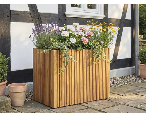 Ghiveci dreptunghiular mare din șipci de lemn, plantat cu lavandă și mușcate, pe o terasă în fața unei fațade cu paiantă.