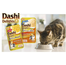 Scenă luminoasă cu pliculețe CIAO Dashi Delights, rețete de pui Silky Broth și Delicate Flakes, și o pisică mâncând dintr-un bol.