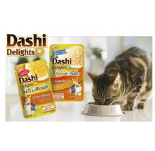 Pisică mâncând dintr-un bol lângă hrana pentru pisici Dashi Delights Chicken Recipe Silky Broth și Delicate Flakes.