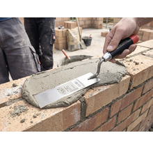 O mână aplică mortar pe un zid de cărămidă cu o mistrie de zidar pe un șantier.