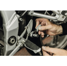 O persoană utilizează un clichet mic cu cheie tubulară pentru întreținere la cadrul unei motociclete.