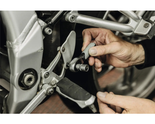 O persoană utilizează un clichet mic cu cheie tubulară pentru întreținere la cadrul unei motociclete.
