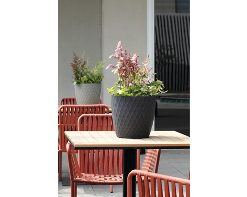 Ghiveci de flori gri închis cu model de romburi și flori roz pe o masă de grădină la exterior.