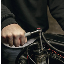 Mână care utilizează un clichet mic cu mâner gri pe o piesă de motor.