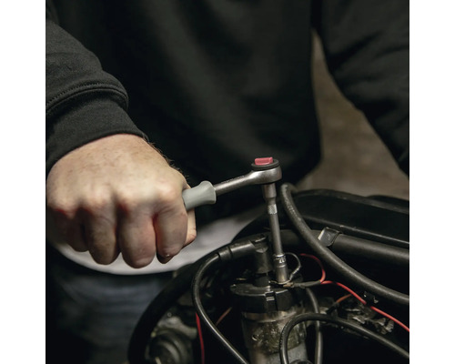 Mână care utilizează un clichet mic cu mâner gri pe o piesă de motor.