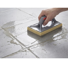 Curățarea plăcilor de gresie cu o drișcă cu burete cu mâner gri și burete galben după rostuire.