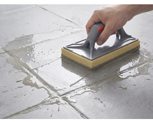 Curățarea plăcilor de gresie cu o drișcă cu burete cu mâner gri și burete galben după rostuire.