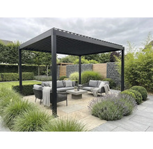 Pergolă modernă din aluminiu cu lamele deasupra unui set de mobilier gri pentru grădină, pe o terasă din piatră, înconjurată de plante.