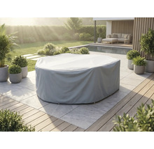 Husă gri de protecție pentru set rotund de mobilier de grădină pe o terasă din piatră deschisă la culoare într-o grădină cu piscină.