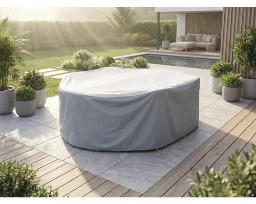 Husă gri de protecție pentru set rotund de mobilier de grădină pe o terasă din piatră deschisă la culoare într-o grădină cu piscină.