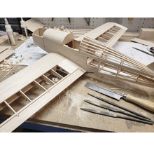 Construcția unui model de avion din lemn pe un banc de lucru cu unelte precum fierăstrău fin, pile ac și adeziv pentru lemn.