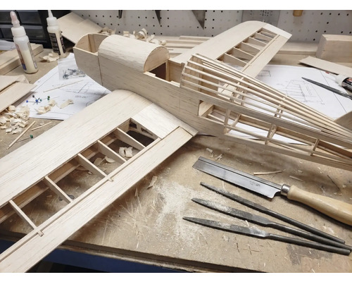 Construcția unui model de avion din lemn pe un banc de lucru cu unelte precum fierăstrău fin, pile ac și adeziv pentru lemn.