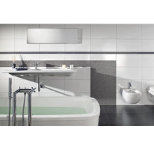 Baie modernă cu cadă albă, lavoar suspendat și bidet, mozaic gri și plăci ceramice albe de mari dimensiuni pentru perete.