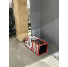 Capcană cu lipici pentru șoareci și șobolani sub formă de tunel amplasată pe podea lângă un stâlp de lemn.
