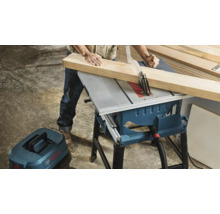 Persoană tăind lemn cu un ferăstrău cu masă Bosch într-un atelier, cu aspirator Bosch conectat pentru praf.