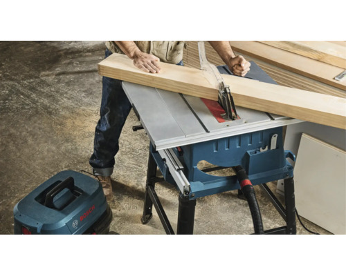 Persoană tăind lemn cu un ferăstrău cu masă Bosch într-un atelier, cu aspirator Bosch conectat pentru praf.