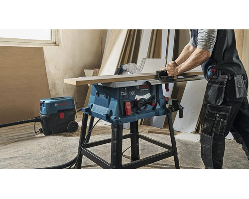 Fierăstrău circular cu masă Bosch Professional GTS 254 tăind lemn cu un aspirator universal Bosch conectat într-un atelier.