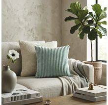 Sufragerie modernă cu o pernă decorativă din catifea raiată verde mentă și o pernă tricotată bej pe o canapea din material textil neutru.